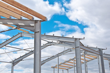 Metal frame of the new building against the blue sky with clouds. Metal frame of the building for further insulation. Wood beams and metal frame of the new building. 