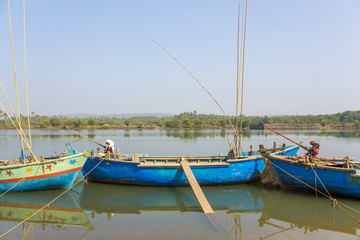 old large fishing boats with engines anchored off the coast against the backdrop of a river and green trees on the shore