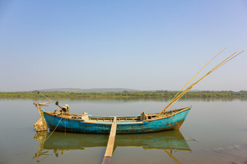 a big old fishing boat with a motor and fishing rods anchored with a ladder at the shore against the backdrop of a river and green forest