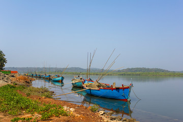 Obraz premium large old fishing boats with motors and fishing rods anchored off the coast against the backdrop of a river and green forest