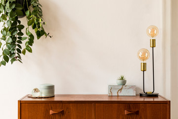 Stylish and design space of home interior with vintage cupboard, marble elegant accessories, hanging plant and gold table lamp. Cozy home decor. Minimalistic concept. Copy space. Real photo, Template.