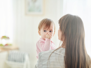 Curious baby girl held by her mother sucking thumb while looking at something interesting, copy...