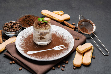 Classic tiramisu dessert in a glass and cup of coffee on dark concrete background