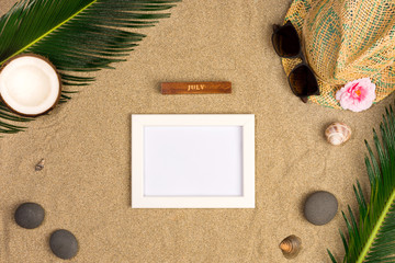 Fototapeta na wymiar Sunglasses, hat, palm leaves and photo frame on sand beach beckground, summer travel concept