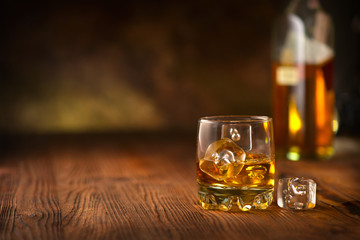 Whisky on the rocks. Glass of whiskey with ice cubes over dark wooden background