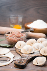 Fototapeta na wymiar Raw dumplings on the cutting board and ingredients for their preparation: flour, egg, minced meat on a wooden table