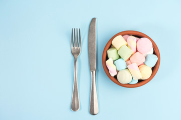 Fototapeta na wymiar Marshmallows in a round bowl, fork, knife isolated on blue background. Top view.