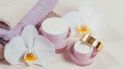 Bottles of hand or face cream or facial mask, towels and white orchid flowers on light background.