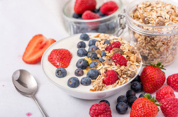 White yogurt in bowl with oatmeal and strawberries, blueberries and raspberries on the top on white background