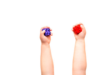 Child is holidng violet and red constructor blocks in fists. Kid's hands with toy on white background. Flat lay, top view.