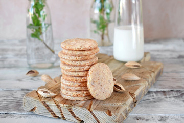 Round almond cookies on the wooden board and a bottle of milk in the background