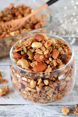 Granola with different nuts in a glass jar on the white wooden table