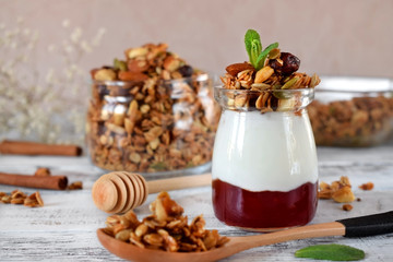Layered breakfast with granola, yogurt and jam in a glass jar on the white table