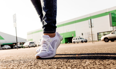 Plakat Woman in white sneakers standing on asphalt road towards sun, close up