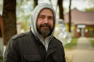 A man with a beard in the hood in the park.