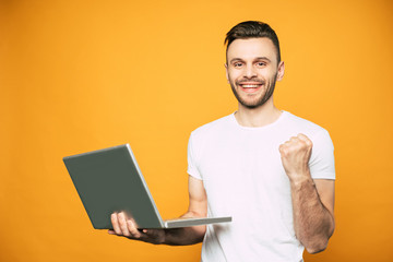 Happy and excited man in white t shirt with laptop in hands on yellow background