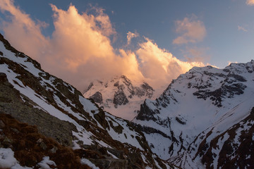 mountain peaks covered with snow with bright clouds in the evening at sunset against the blue sky. Kabardino-Balkaria, Russia