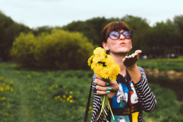 Young pretty woman with yellow dandelions in the sunny summer park.