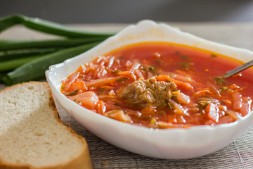 Ukrainian beetroot soup - borscht in a white bowl on the kitchen table. Delicious beet soup. Fresh borsch on the table surrounded by products