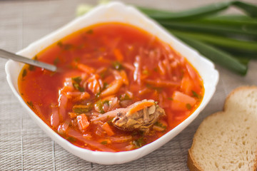 Ukrainian beetroot soup - borscht in a white bowl on the kitchen table. Delicious beet soup. Fresh borsch on the table surrounded by products