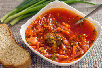 Ukrainian beetroot soup - borscht in a white bowl on the kitchen table. Delicious beet soup. Fresh borsch on the table surrounded by products
