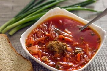 Ukrainian beetroot soup - borscht in a white bowl on the kitchen table. Delicious beet soup. Fresh borsch on the table surrounded by products