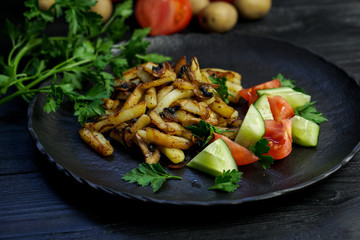 Fried potatoes with mushrooms and onions. Tomatoes,parsley and cucumbers on a plate
