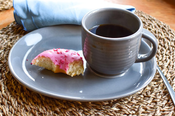 A cup of coffee and a bitten donut are on the table. Dessert with coffee.