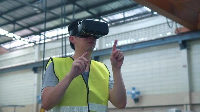 Industrial factory and manfacturing engieering worker wearing VR goggle headset touching in virtual reality simulation alongside heavy duty machines