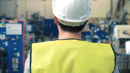 Close up rear view of factory worker with safety hard hat is walking through industrial facilities at heavy industry manufacturing factory