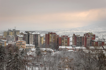 Idyllic winter cityscape, warm colors of the buildings, foreground trees covered with snow and soft sunset sky
