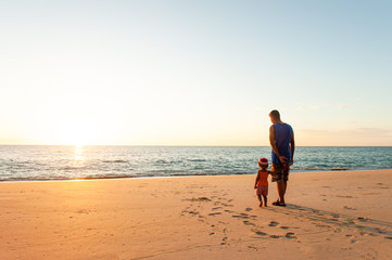 A little girl holding her father hands on the sunset beach.
