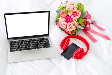 Laptop computer isolated white screen for mockup design and display with headphones, cell phone and flower bouquet on white fabric quilt