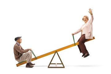 Senior man and woman waving and sitting on a seesaw