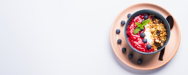Yogurt smoothie bowl with blended raspberries, blueberries and oat matcha granola on pastel background. Delicious healthy breakfast concept