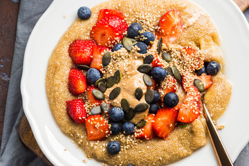 Gluten free amaranth topped with homemade almond butter, fresh strawberries, sesame, pumpkin seeds. Vegan plant based breakfast served on dark wooden board. Healthy colorful food concept.