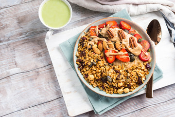 Delicious amaranth porridge topped with home made granola, strawberries and almond butter. Vegan plant based breakfast served with matcha latte on white wooden board. Healthy colorful food concept