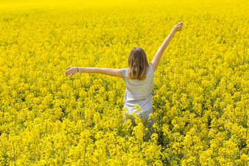 Beautiful young girl enjoys the scent of yellow flowery field.