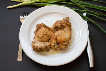 Fried spicy chicken with green onions on a white plate with cutlery. Isolated on black