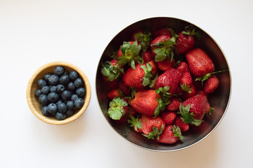 Small wooden bowl with blueberries stands next to a large strawberry bowl.