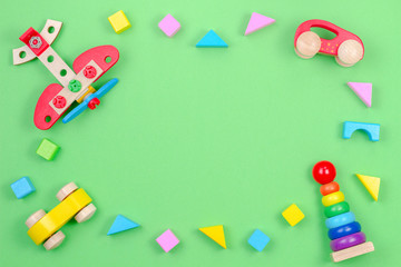 Kids toys background frame with wooden plane, cars, baby stacking rings pyramid and colorful blocks on green background
