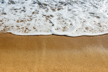 Close-up view of foamy, curvy sea wave on a wet, golden sand
