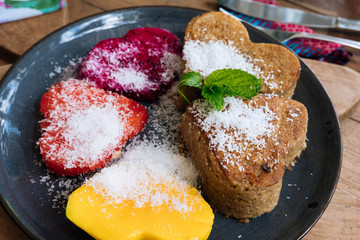 Close up Oatmeal Pancakes and tropical fruits in the form of a heart with mint and honey on wooden table. Valentine's Day. Healthy food concept. Top view.