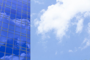 Fototapeta na wymiar Blue windows of a building with clouds reflected in them against a cloudy sky
