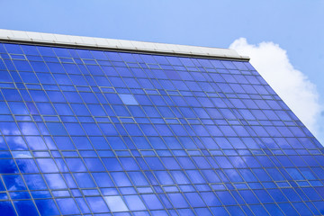 Fototapeta na wymiar Blue windows of a building with clouds reflected in them against a cloudy sky