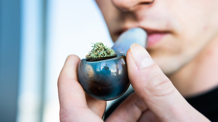 glass pipe for smoking marijuana. A man holds in his hand a tube with marijuana buds before use