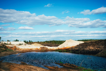 Industrial sand quarry with artificial reservoir. Sand pit. Construction industry. Sand hills agains the blue sky.