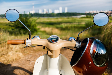 A first-person view of the steering wheel of a classic vintage moped with a beautiful helmet with a...