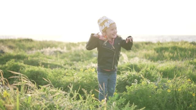 Fashionable little girl walks in the park by the sea. Baby jumps in the tall grass and laughs. Walk by the sea in spring. Happy child playing on the beach. Spring Cyprus with children