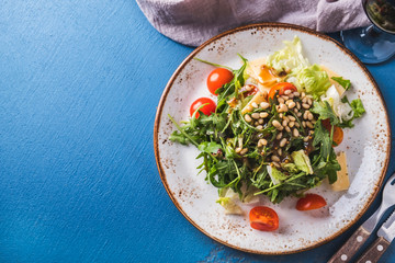 Arugula healthy salad with  pine nuts, tomatoes and cheese. Top view. Copy space